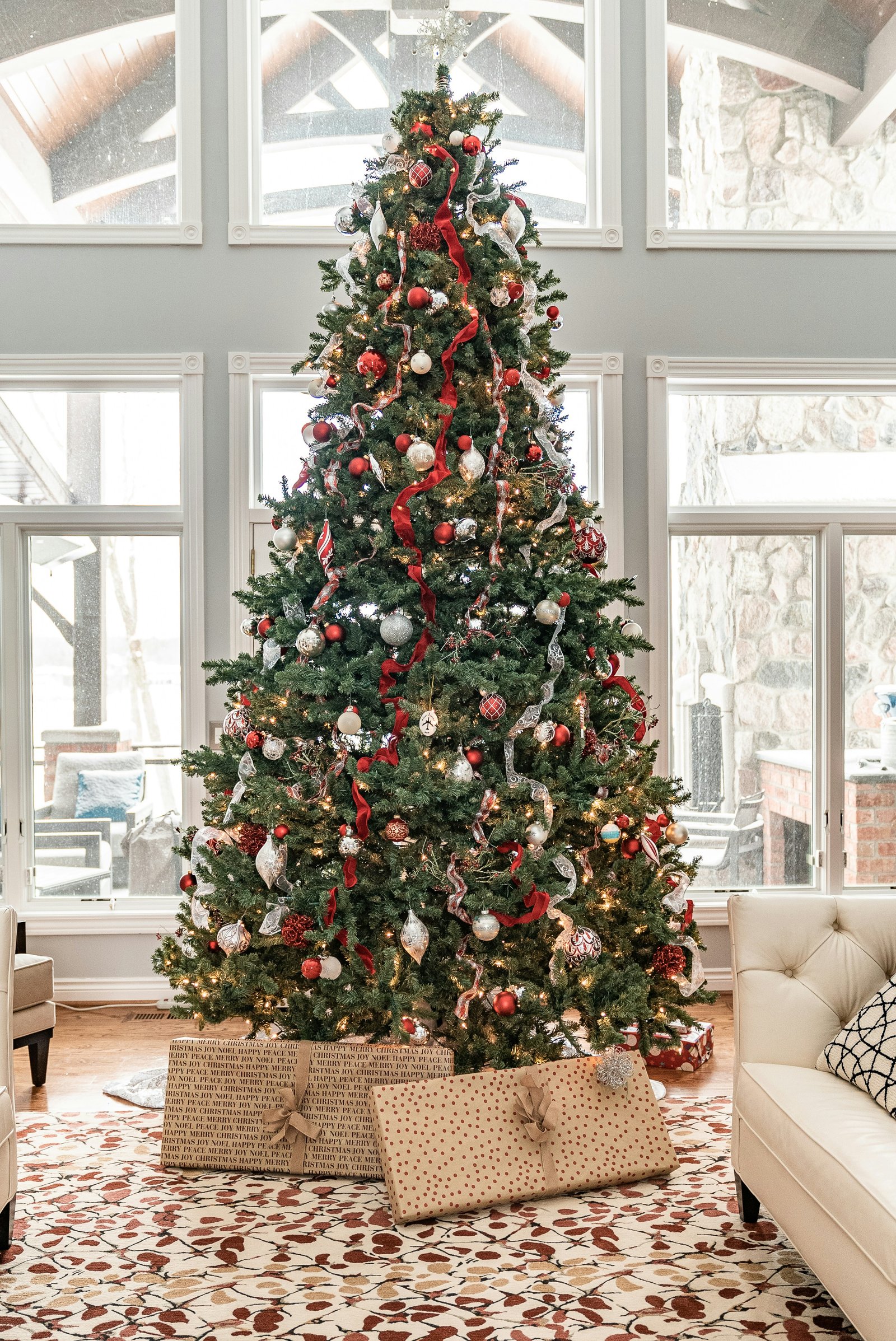 A tall Christmas tree with red ribbon and ornaments, with wrapped gifts beneath